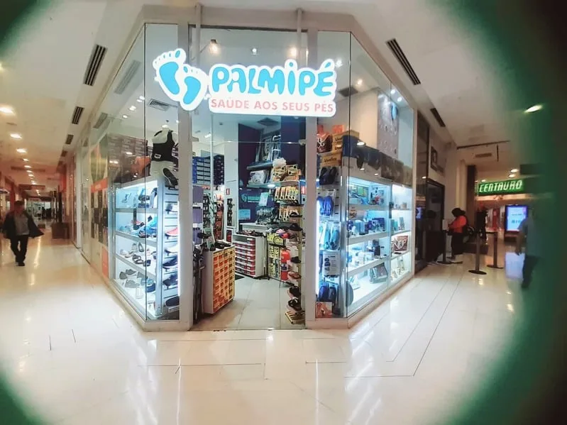 Vista externa da loja Palmipé no corredor do shopping, com vitrine iluminada e movimento de clientes